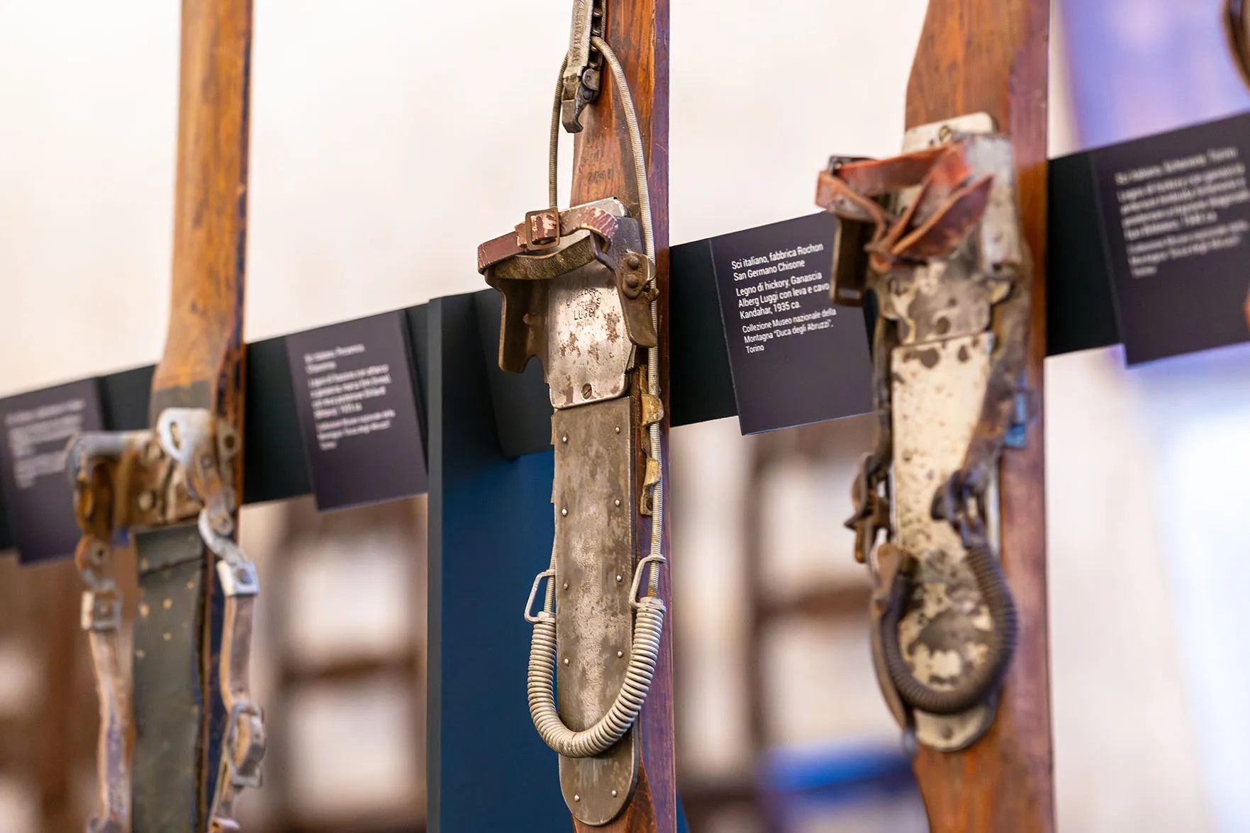 Dettaglio degli sci esposti nel Salone d’Onore: nell’immagine si vedono 3 sci d’epoca di produzione italiana (dal 1925 al 1940 circa), provenienti dalle collezioni del Museo Nazionale della Montagna “Duca degli Abruzzi” - Torino. Lo sci centrale (1935) in legno di hickory monta attacchi Kandahar con cavo a molla metallico e leva anteriore di serraggio.